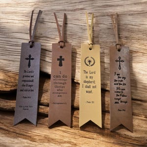 May include: Four brown leather bookmarks with different bible verses and cross designs. The verses are: "The Lord is gracious and compassionate, slow to anger and rich in love." - Psalm 103:8, "I can do all things through Christ who strengthens me." - Philippians 4:13, "The Lord is my shepherd; I shall not want." - Psalm 23:1, "I am the way, the truth, and the life. No one comes to the Father except through me." - John 14:6