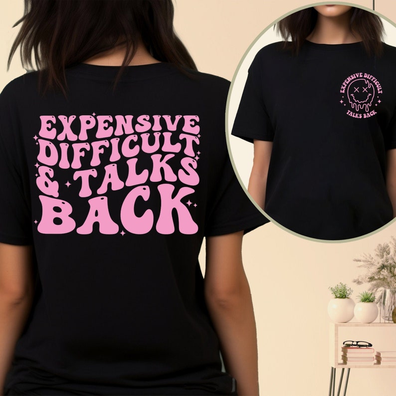 May include: Black t-shirt with pink text on the back that reads "Expensive Difficult & Talks Back". The front of the shirt has a pink graphic of a melting smiley face with the text "Expensive Difficult Talks Back".