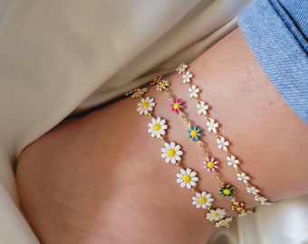 May include: Four gold chain anklets with white daisy charms. The daisies have yellow centers and are accented with different colored enamel: pink, teal, green, and red.