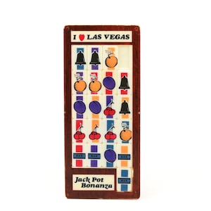May include: A rectangular wooden Las Vegas souvenir featuring a slot machine design. The design includes various fruit and bell symbols, with the text "I ❤️ LAS VEGAS" at the top and "Jack Pot Bonanza" at the bottom. The frame is brown.