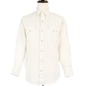 May include: Off-white long-sleeve shirt with a classic Western design. Features two chest pockets with silver snap closures, a pointed collar, and snap closures down the front. The shirt is displayed on a mannequin.