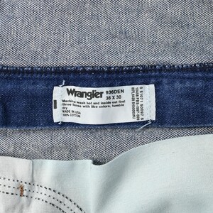 May include: Close-up of a pair of Wrangler jeans. The label reads "Wrangler 936DEN 36 X 30" and "MADE IN USA 100% COTTON". The jeans are a dark blue denim with a light blue interior.