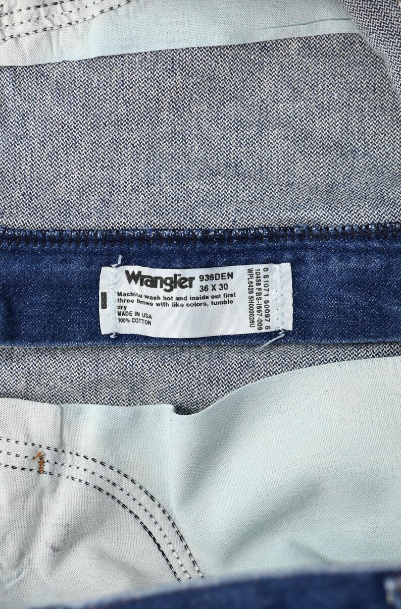 May include: Close-up of a pair of Wrangler jeans. The label reads "Wrangler 936DEN 36 X 30" and "MADE IN USA 100% COTTON". The jeans are a dark blue denim with a light blue interior.