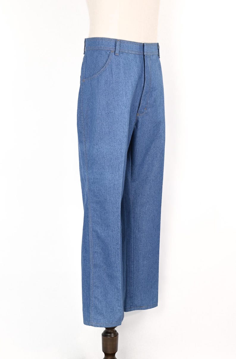 May include: Light blue denim jeans with a straight leg cut. The jeans have a classic five-pocket design and a button and zip closure. The jeans are displayed on a mannequin.