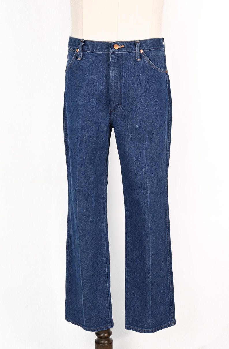 May include: Dark blue denim jeans with a classic five-pocket design. The jeans have a straight leg cut and a button and zipper closure. The fabric appears to be a medium weight denim. The jeans are displayed on a mannequin.