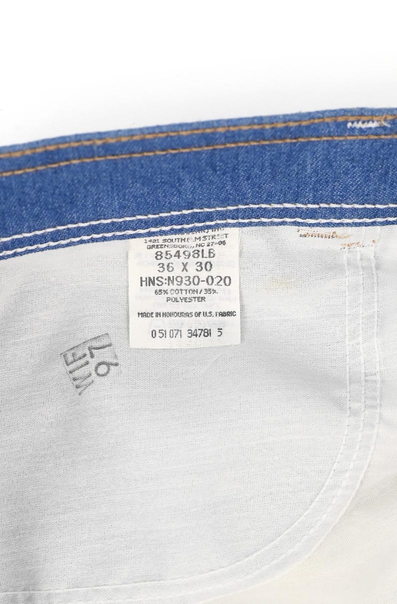 K&ouml;nnte beinhalten: Nahaufnahme der Innenseite einer blauen Jeans. Ein wei&szlig;es Etikett ist in den Stoff eingen&auml;ht und zeigt die Gr&ouml;&szlig;e 36 x 30 sowie weitere Details. Die Jeans besteht aus 65 % Baumwolle und 35 % Polyester.