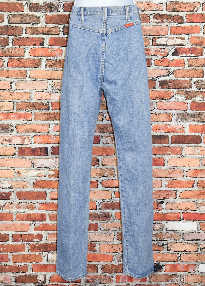Peut inclure: Un jean en denim bleu clair &agrave; taille haute et &agrave; jambe droite. Le jean a une braguette &agrave; boutons et des passants de ceinture.