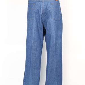 May include: Light blue denim jeans with a classic five-pocket design. The jeans have a straight leg cut and a high waist. The back pockets are square. The Wrangler logo is visible on the back pocket.