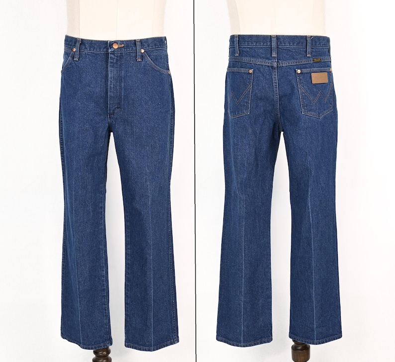 May include: A pair of blue denim jeans, displayed front and back. The jeans have a classic five-pocket design, a button and zipper closure, and a flared leg. The back features two pockets and a brown leather patch.