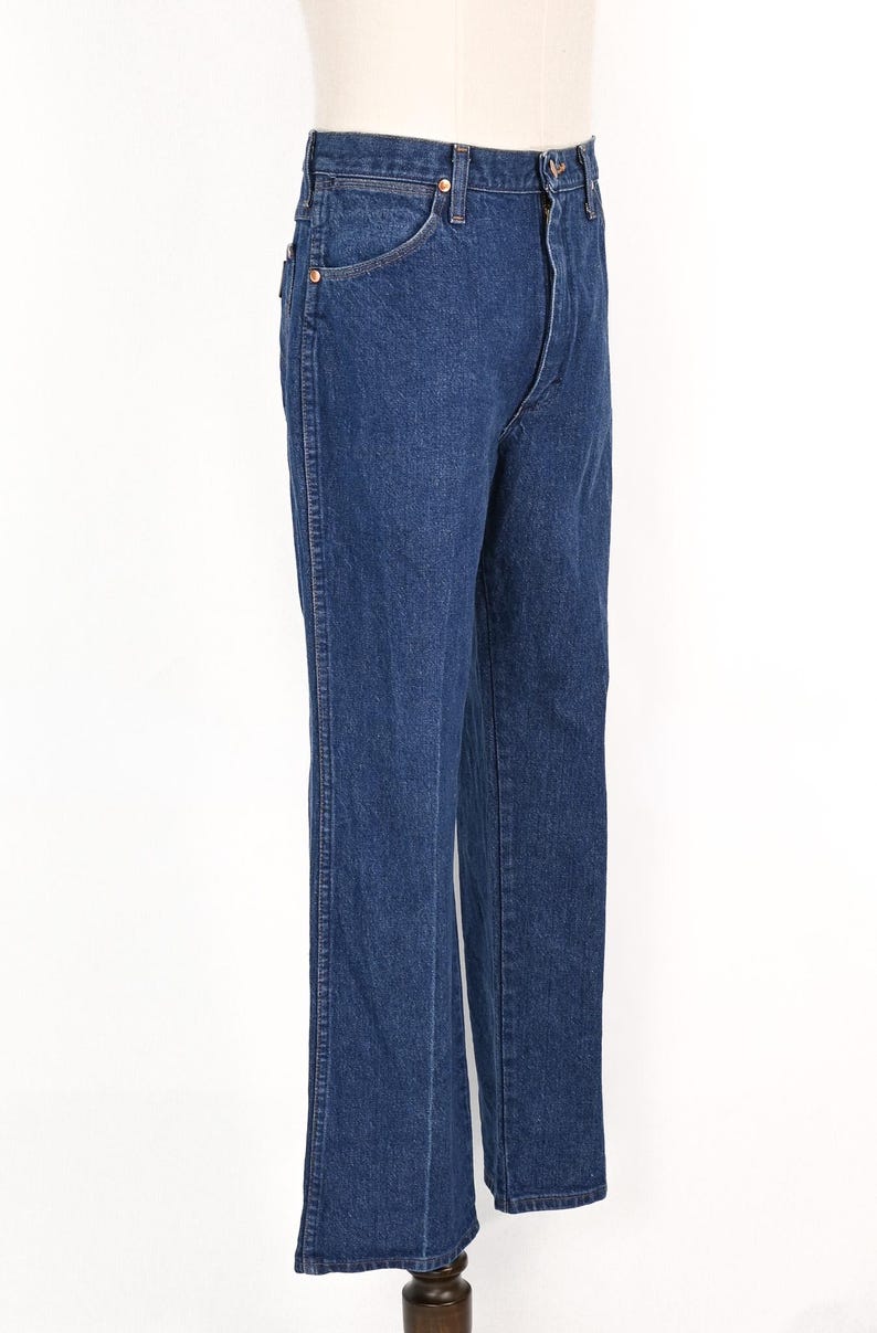 May include: Dark blue denim jeans with a classic straight leg fit. The jeans have a button and zipper closure, front and back pockets, and belt loops. The jeans are displayed on a mannequin.