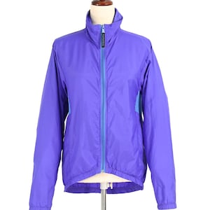 May include: A purple jacket with a high collar and a full-length zip. The jacket has blue panels on the sides and a blue zip. The jacket is displayed on a mannequin.
