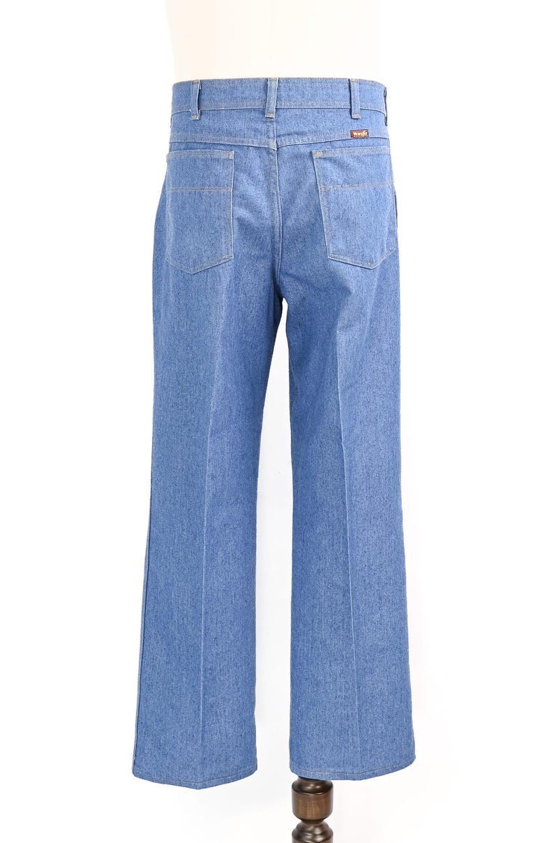 K&ouml;nnte beinhalten: Hellblaue Jeans mit weitem Bein. Die Jeans hat zwei Ges&auml;&szlig;taschen und ein kleines braunes Etikett auf der R&uuml;ckseite. Die Jeans wird auf einer Schaufensterpuppe pr&auml;sentiert.