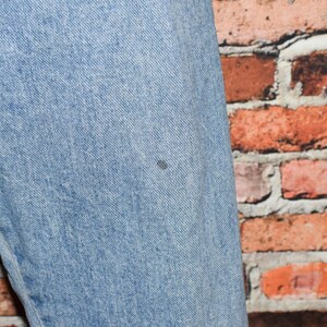 Peut inclure: Gros plan sur un tissu en jean bleu clair avec une petite tache sombre. Le tissu est textur&eacute; et a un aspect d&eacute;lav&eacute;.