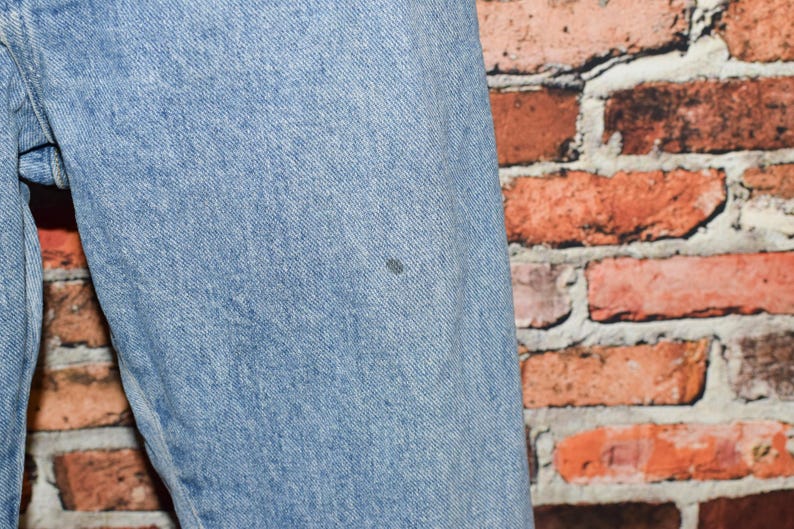 Peut inclure: Gros plan sur un tissu en jean bleu clair avec une petite tache sombre. Le tissu est textur&eacute; et a un aspect d&eacute;lav&eacute;.