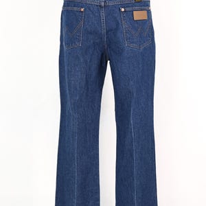 May include: Dark blue denim jeans with a classic five-pocket design. Features a brown leather patch and the Wrangler logo on the back pocket. The jeans have a straight leg and are displayed on a mannequin.