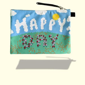 May include: A rectangular pouch with a cheerful design. The pouch features a blue sky background with white cloud-shaped letters spelling "HAPPY" and a field of flowers. A yellow sun is in the upper right corner. The pouch has a black wrist strap and zipper.