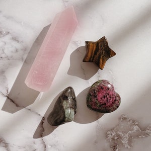 Pode incluir: Uma cole&ccedil;&atilde;o de quatro cristais: uma ponta de quartzo rosa rosa, uma estrela de olho de tigre marrom, um cristal em forma de cora&ccedil;&atilde;o verde e preto e um cristal em forma de cora&ccedil;&atilde;o rosa e verde.