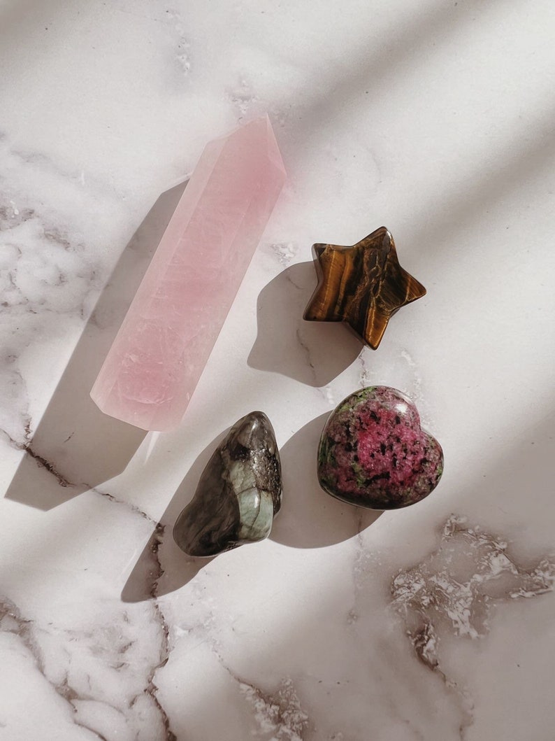 Pode incluir: Uma cole&ccedil;&atilde;o de quatro cristais: uma ponta de quartzo rosa rosa, uma estrela de olho de tigre marrom, um cristal em forma de cora&ccedil;&atilde;o verde e preto e um cristal em forma de cora&ccedil;&atilde;o rosa e verde.