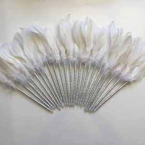 May include: A set of 20 white feathers attached to silver pens. The feathers are arranged in a fan shape.