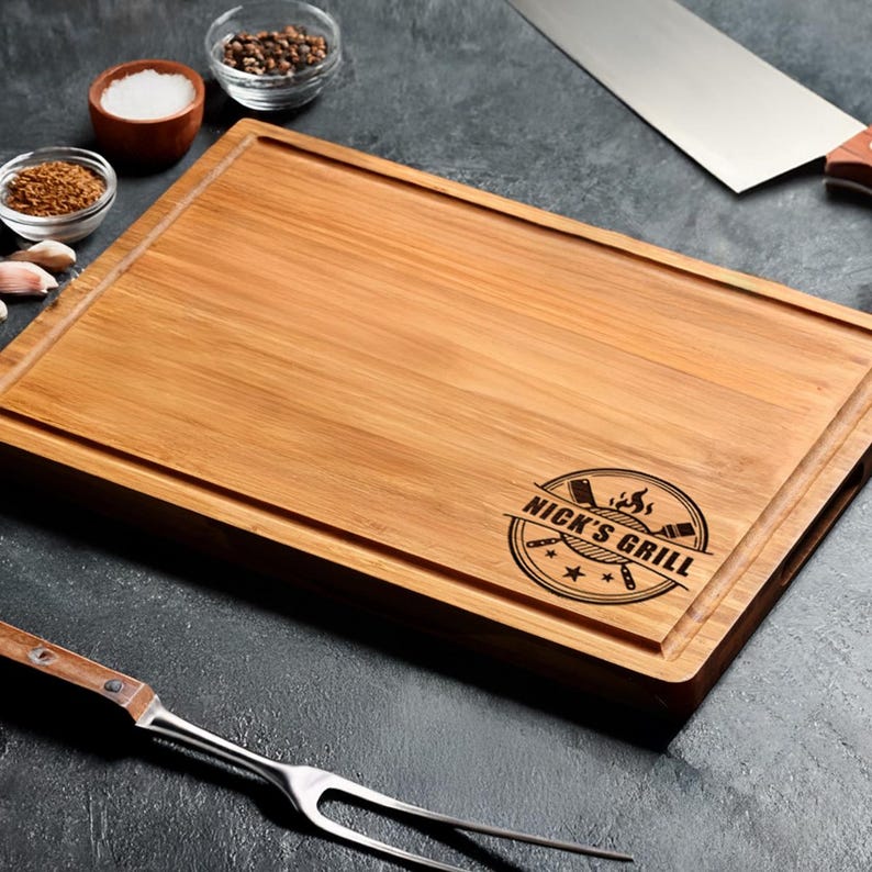 A wooden cutting board with a logo, knife, and various cooking utensils on a dark surface.