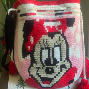 Puede incluir: Un bolso tipo saco de ganchillo cil&iacute;ndrico con un gr&aacute;fico pixelado de un rat&oacute;n de dibujos animados con un gorro rojo. El bolso est&aacute; hecho con hilo blanco, rojo, negro y beige, incluye un cierre de cord&oacute;n blanco y borlas de hilo rojo.