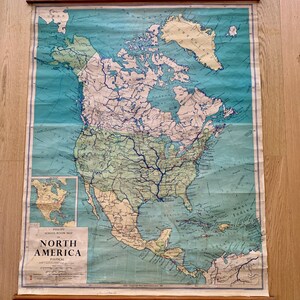 May include: A vintage, rolled-up map of North America with a blue background and brown borders. The map is titled "PHILLIPS SCHOOL ROOM MAP NORTH AMERICA POLITICAL" and includes a smaller inset map of the United States.
