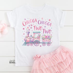 May include: White toddler t-shirt with a colorful train graphic and the text "Chugga Chugga Two Two." A pink tulle skirt and a pink bow are also in the image. The train is decorated with flowers and hearts.