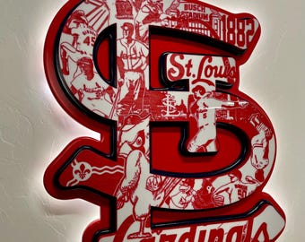 May include: A red, white, and black illuminated sign in the shape of the St. Louis Cardinals logo. The sign features the team's name, the city name, and images of baseball players. The year 1882 is also visible.