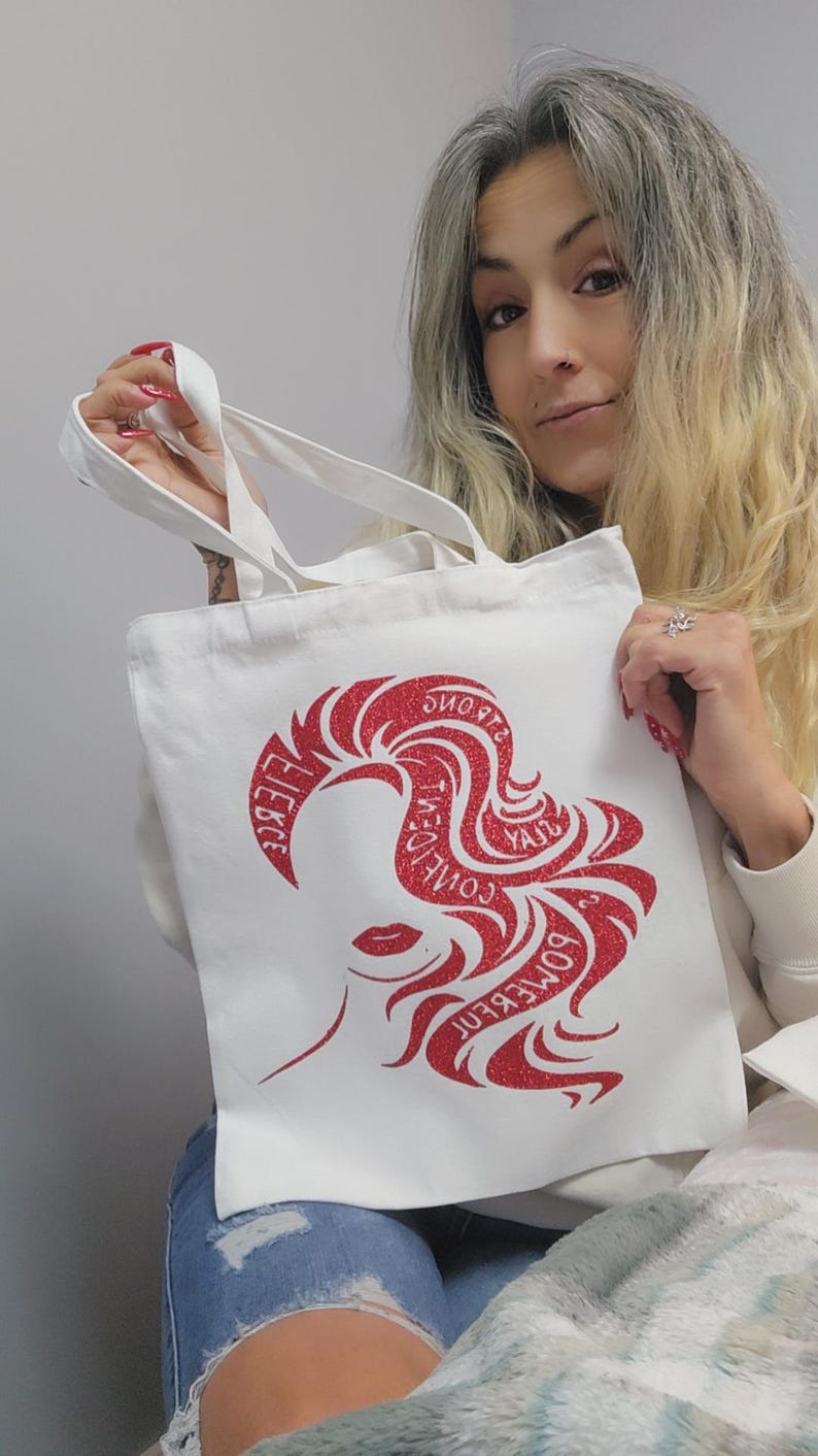 May include: White tote bag featuring a red glitter design of a woman's silhouette and the words "Some Kind of Wonderful" and "Fierce". The bag has white handles and is made of a durable fabric.