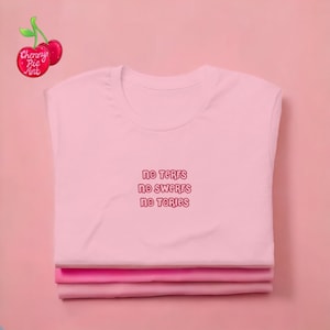 May include: Pink t-shirt with the text "NO TERFS NO SWERFS NO TORIES" printed in pink on the front.