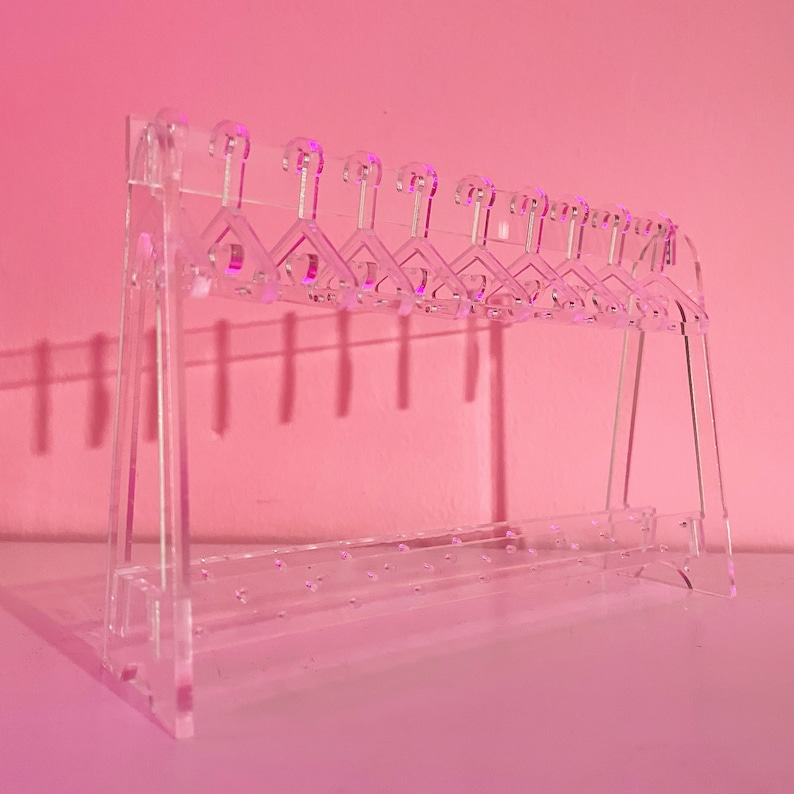 May include: A clear acrylic earring holder with multiple hooks and a bottom shelf with holes for storing earrings.