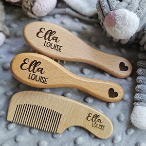 May include: Three wooden baby grooming tools: two brushes and a comb. The brushes have an oval head and a handle, with the name "Ella LOUISE" engraved on them. A heart is engraved on the handle of one brush. The comb has the same name engraved on it.