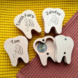 Puede incluir: Cuatro cajas de madera para el hada de los dientes con diseño de diente. Cada caja tiene un nombre diferente y un diseño de hada. Una caja tiene una moneda dentro.