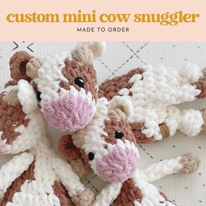 Pode incluir: Tr&ecirc;s peluches de vaca de croch&ecirc; em marrom, branco e rosa. Os peluches t&ecirc;m um padr&atilde;o de manchas e s&atilde;o feitos com um fio macio e felpudo. Os peluches est&atilde;o dispostos em um fundo branco com um padr&atilde;o de diamantes.