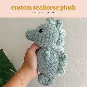 May include: A soft, green and white crocheted seahorse plush toy. The seahorse has a textured, fluffy surface and a cute, cartoon-like face.