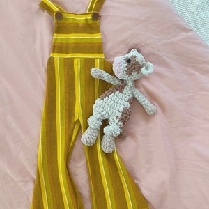 Pode incluir: Macac&atilde;o listrado amarelo e marrom com um bot&atilde;o marrom nas al&ccedil;as. Um brinquedo de pel&uacute;cia de vaca marrom e branco de croch&ecirc; est&aacute; em cima do macac&atilde;o.