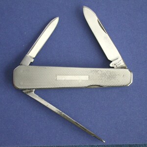 May include: A silver pocket knife with three open blades against a blue background. The knife has a textured handle and a small rectangular indentation. The blades are shiny and sharp.