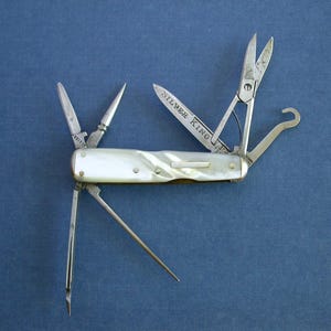 May include: A classic multi-tool with a mother-of-pearl handle and several folding tools, such as scissors, a knife, and a hook. The blade is marked "SILVER KING". The tool is open, showing its functions against a blue backdrop.