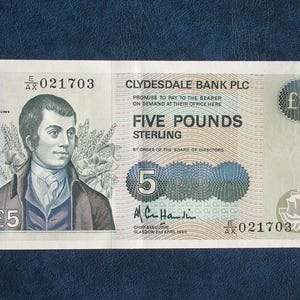 May include: A five-pound note from Clydesdale Bank PLC, featuring a portrait of Robert Burns. The note displays the text "FIVE POUNDS STERLING" and the denomination "£5". The serial number is visible.