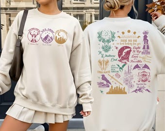 May include: Cream-colored sweatshirt with front and back graphic designs. The front features three circular designs with text. The back has a collection of illustrations and text, including a wolf, sword, and the words "There You Are, I've Been Looking For You."