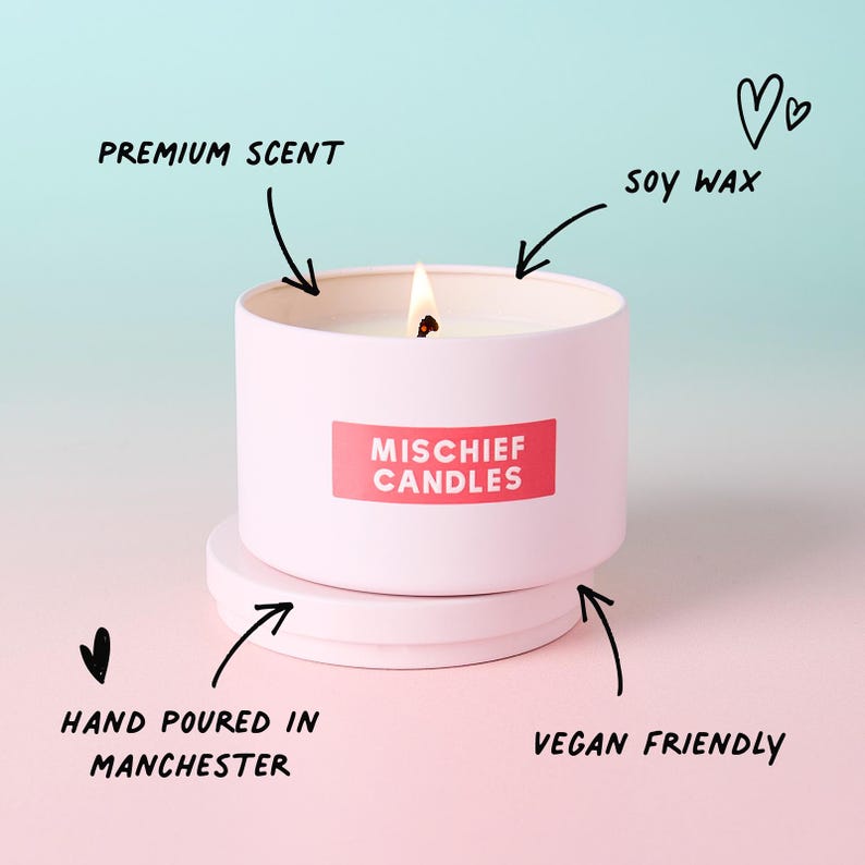 May include: A light pink metal candle tin with a lit wick and a matching lid underneath. A red rectangular label features the white text MISCHIEF CANDLES. Hand-drawn arrows point to the text labels: PREMIUM SCENT, SOY WAX, HAND POURED IN MANCHESTER, and VEGAN FRIENDLY.