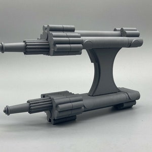 May include: A gray 3D printed model of a spaceship with two long, cylindrical engines and a central body with a raised platform.