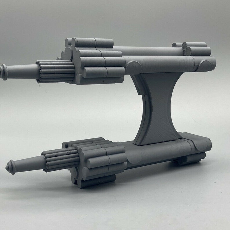 May include: A gray 3D printed model of a spaceship with two long, cylindrical engines and a central body with a raised platform.