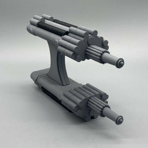 May include: A gray, 3D printed model of a futuristic weapon with a complex design. The weapon has two barrels and a series of cylindrical tubes.