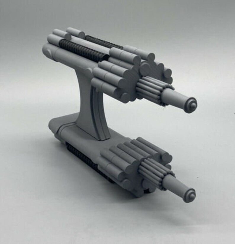 May include: A gray, 3D printed model of a futuristic weapon with a complex design. The weapon has two barrels and a series of cylindrical tubes.