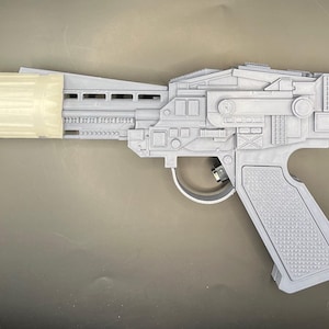 May include: A grey, futuristic blaster pistol with a cylindrical attachment at the end. The pistol has intricate details and a textured grip. The design suggests a science fiction or cosplay prop.