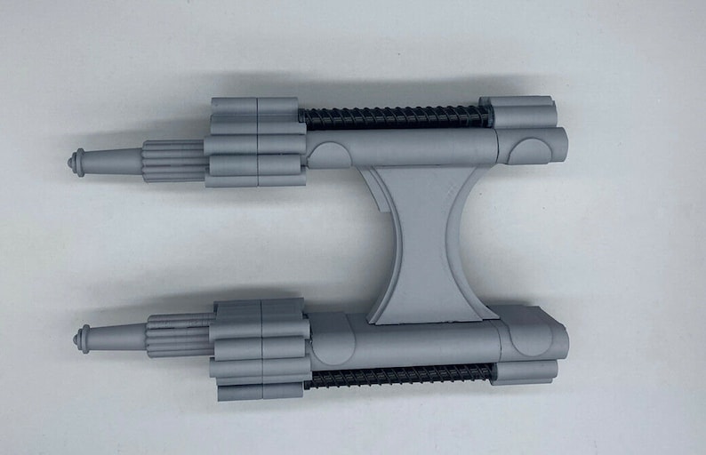 May include: A gray plastic model of a spaceship with two long, cylindrical engines and a central body with a Y-shaped structure.