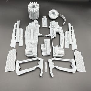 May include: A set of 14 grey plastic pieces for assembling a model gun. The pieces include a barrel, a handle, a trigger, and other parts.