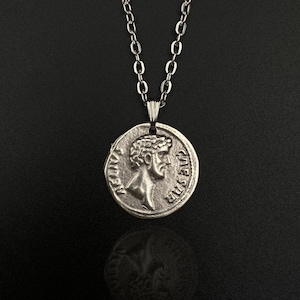 May include: A silver chain necklace with a silver coin pendant featuring a profile of a man's face. The coin has the words "IMP CAESAR" and "CIVES SPQR" inscribed on it.