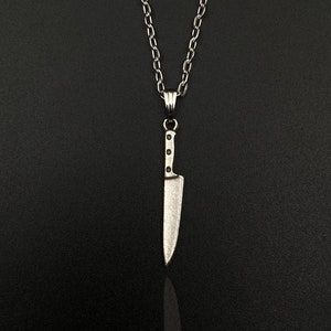 Può includere: Una collana con catena d'argento con un ciondolo a forma di coltello d'argento.